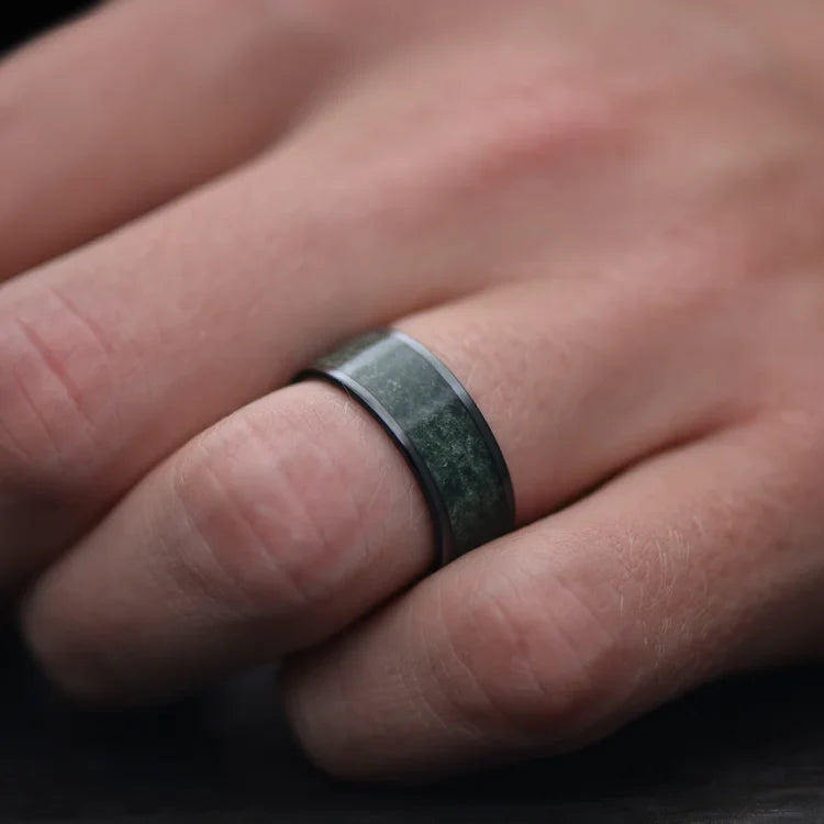 Men's black titanium wedding band with central moss agate inlay, 8mm width, shown on a hand, unique men's ring with free engraving option.