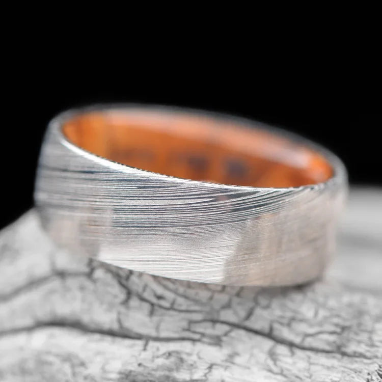 Heimskringla Wedding Band with Olivewood Inner Sleeve, men's 8mm polished domed profile ring, unique design, free engraving, displayed on white sea branch background.