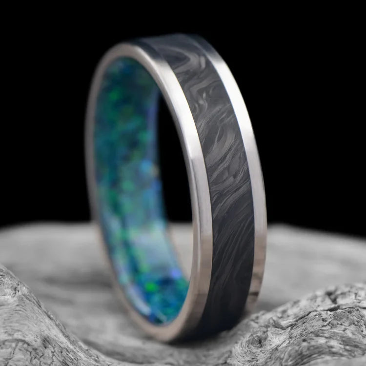 Titanium wedding band with central forged inlay and black emerald opal sleeve, 6mm mens ring, unique design, free engraving, displayed on white sea branch.