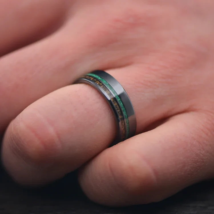 Men's black titanium wedding band with crushed T-Rex and malachite inlays, featuring a whiskey barrel oak inner sleeve, shown on a hand; unique 7mm design with free engraving option.