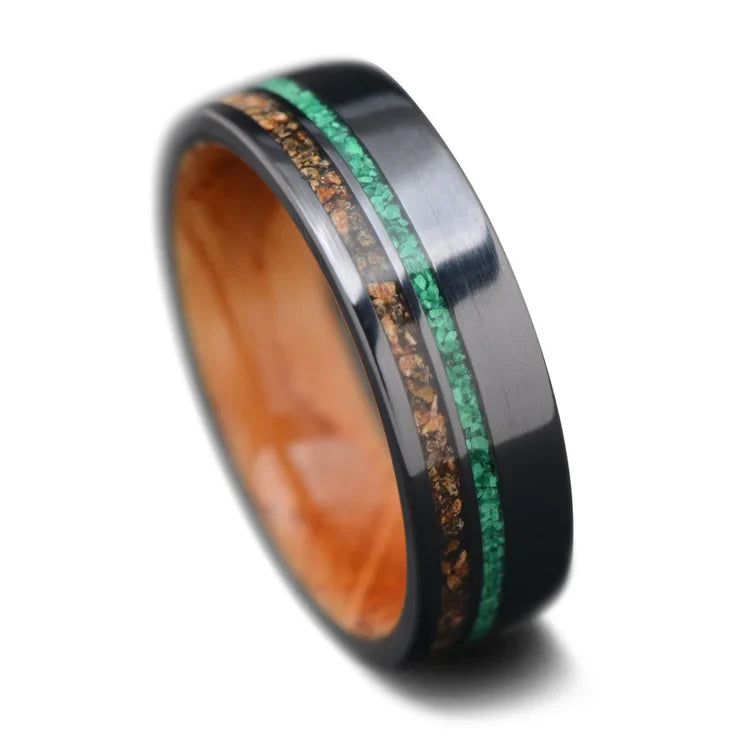 Men's 7mm black titanium wedding band featuring crushed T-Rex and malachite inlays with a whiskey barrel oak inner sleeve, offering free engraving, displayed on a white background.