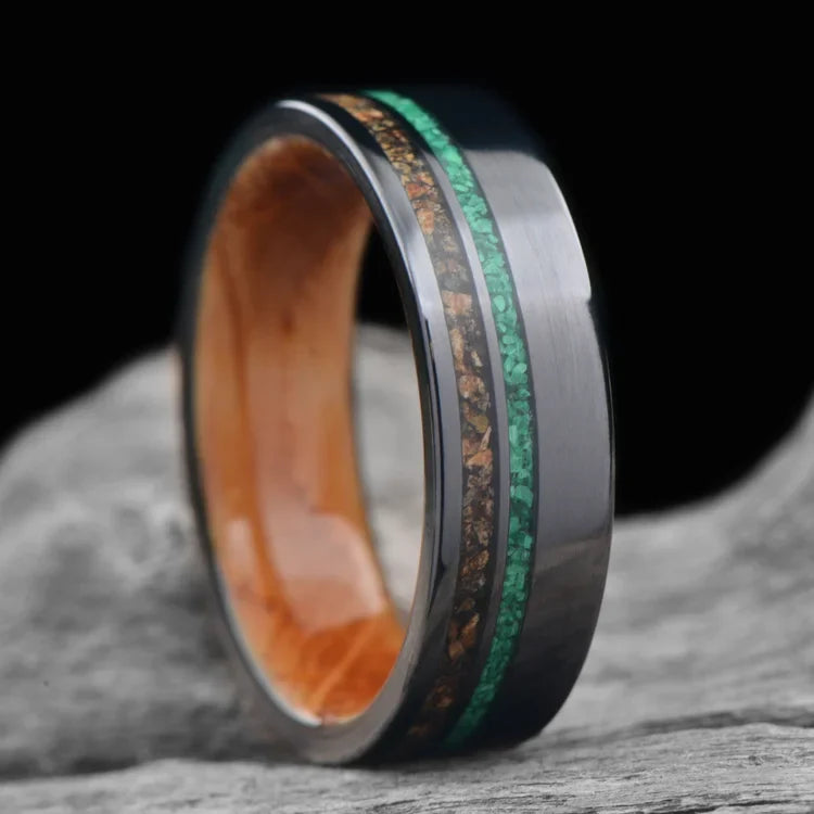 Black titanium wedding band with crushed T-Rex and malachite inlays, featuring a whiskey barrel oak inner sleeve, displayed on a white sea branch, 7mm men's unique ring with free engraving.