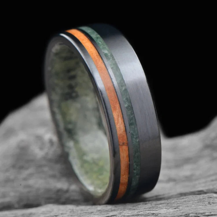 Black Titanium Wedding Band with Western Maple Burl and Moss Agate Inlays, featuring a Jade Inner Sleeve, displayed on a white sea branch; Men's Unique Wedding Ring, 7mm, with Free Engraving Option.