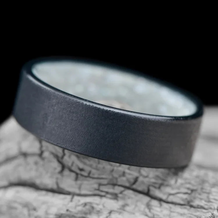 Black Titanium Wedding Band with Granite Finish and Pearl Inner Sleeve, 7mm Mens Wedding Ring, Customizable with Free Engraving, displayed on a white sea branch.