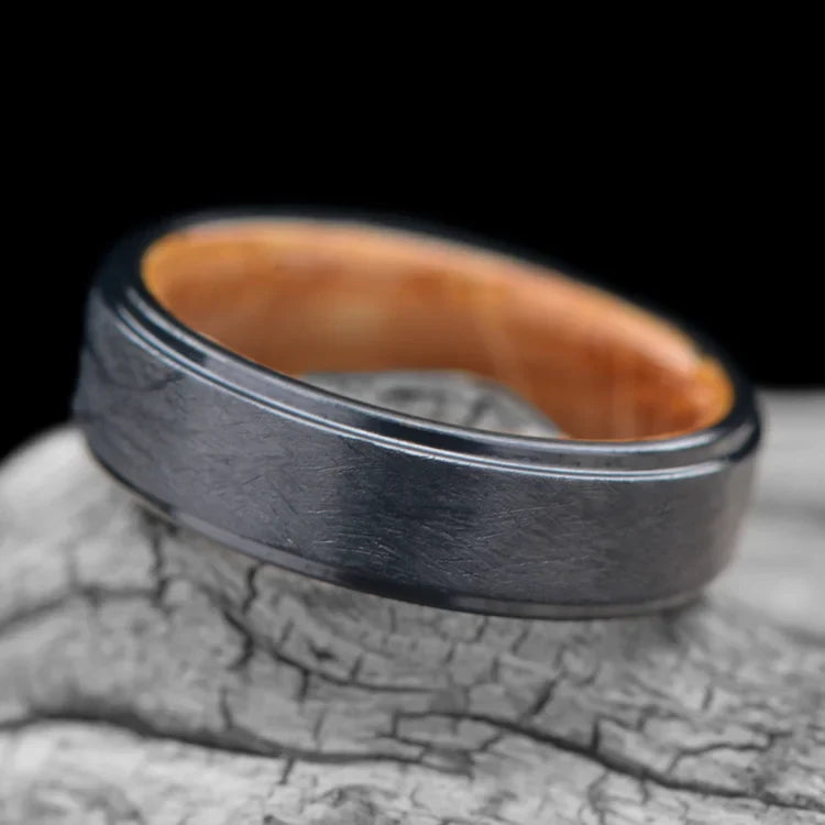 Black Titanium Wedding Band with Whiskey Barrel Oak Inner Sleeve, 6mm Mens Wedding Ring, Brushed Stepped Profile, displayed on a white sea branch, free engraving available.