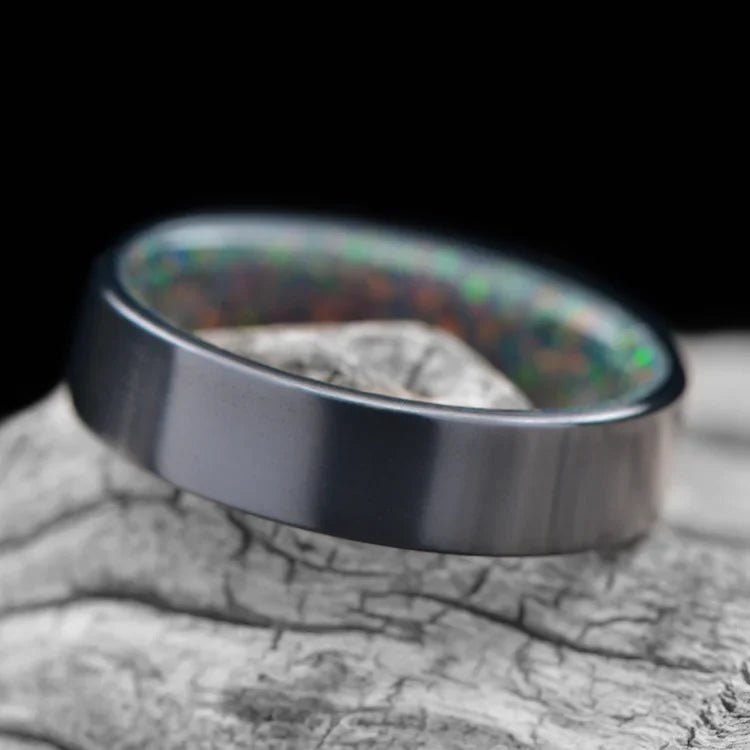 Black Titanium Wedding Band with Black Emerald Opal Inner Sleeve, 6mm Mens Ring, Polished Flat Profile, Free Engraving, displayed on white sea branch.