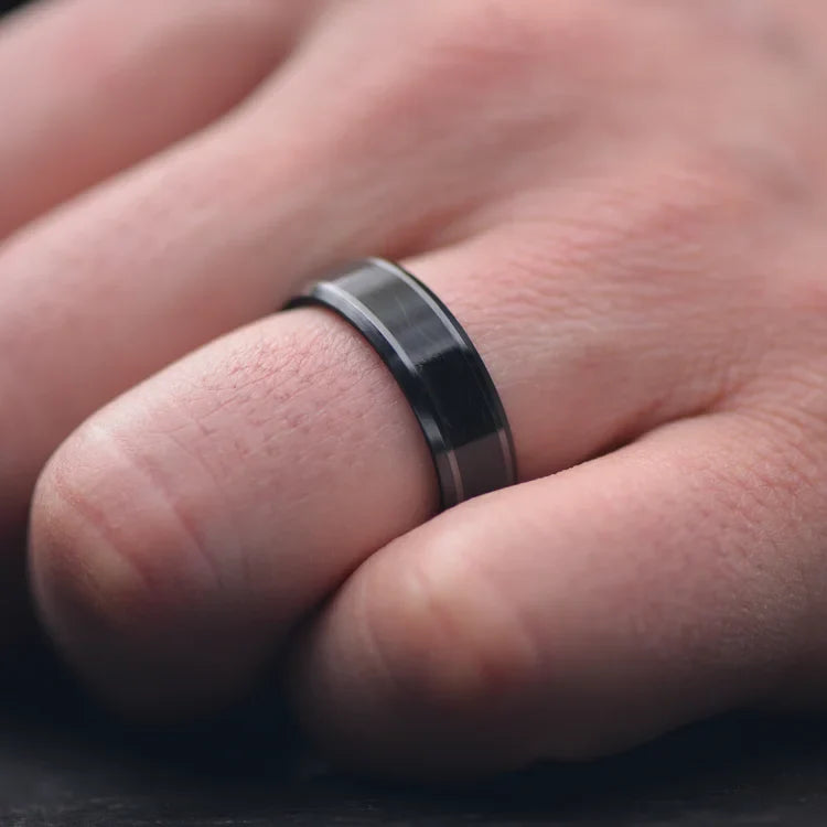 Mens 7mm black titanium wedding band with central forged inlay and black fire opal inner sleeve, shown on a hand, featuring polished finish and free engraving option.