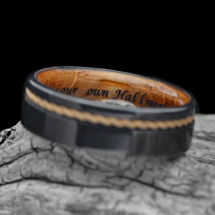 Black titanium wedding band with 10KY rope and whiskey barrel oak inlay, 7mm mens ring, unique design, free engraving, displayed on a white sea branch.