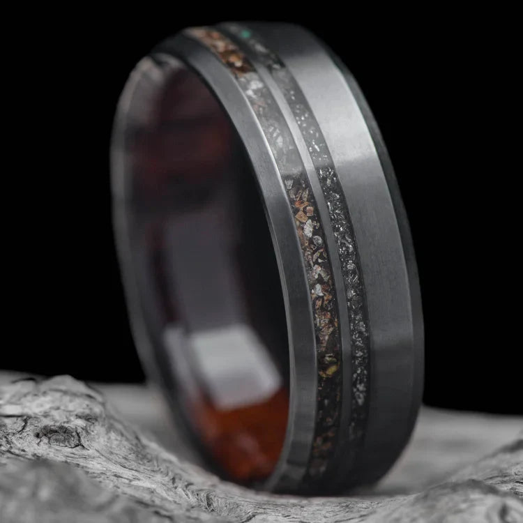 Black titanium wedding band with crushed T-Rex and meteorite inlays, featuring a 7mm mens ring design and a unique WW2 rifle inner sleeve, displayed on a white sea branch.