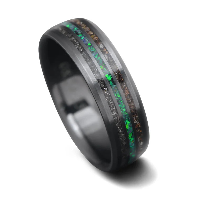 Mens 7mm black titanium wedding band with meteorite and crushed T-Rex inlays, featuring a central black emerald opal, shown on a hand; unique ring with free engraving option.