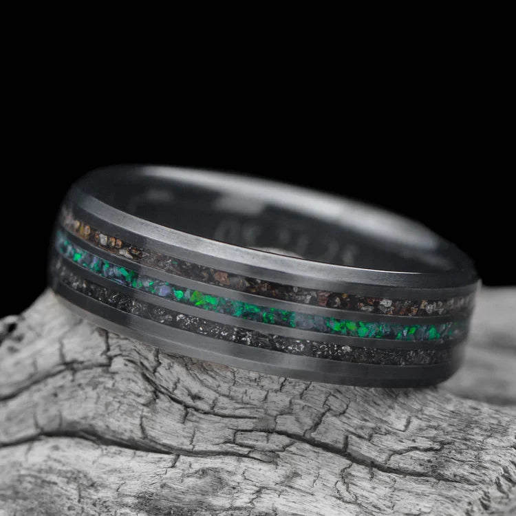 Black Titanium Wedding Band with Meteorite and Crushed T-Rex Inlays featuring a Central Black Emerald Opal, displayed on a white sea branch, 7mm Mens Unique Ring, Free Engraving Available.
