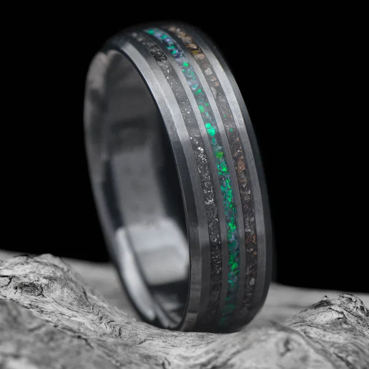 Black titanium wedding band with meteorite and crushed T-Rex inlays, featuring a central black emerald opal, displayed on a white sea branch, 7mm mens unique ring with free engraving.