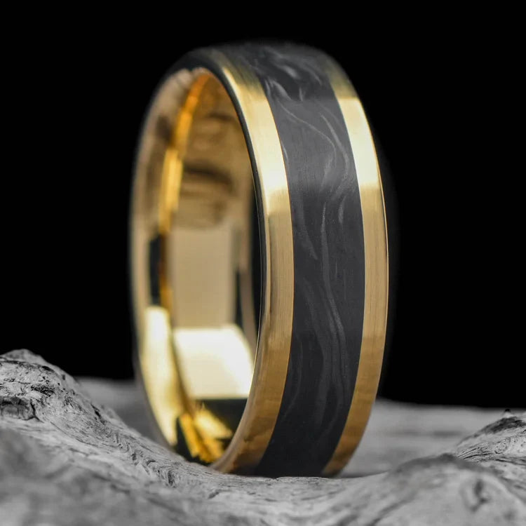 18K yellow gold mens wedding band with central forged inlay, custom brushed flat profile, 6mm wide, offering free engraving, displayed on a white sea branch.