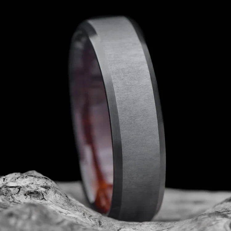 Black titanium wedding band with koa wood inner sleeve, featuring a brushed bevel profile, displayed on a white sea branch; mens 6mm ring with free engraving.