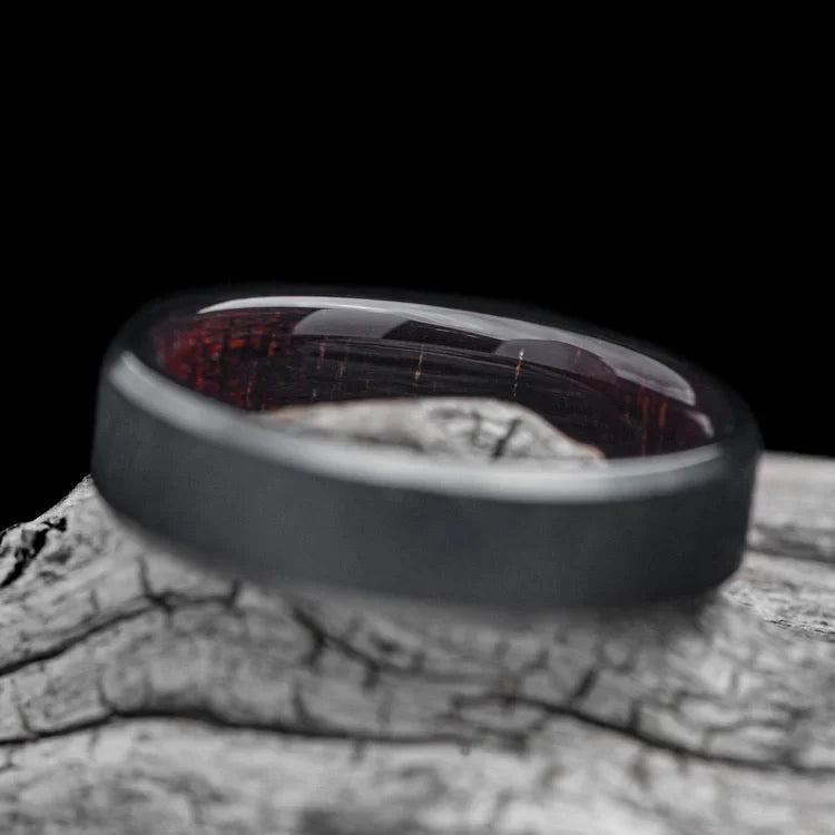 Black titanium wedding band with koa wood inner sleeve, featuring a brushed bevel profile, 6mm mens ring, displayed on a white sea branch, offering free engraving.