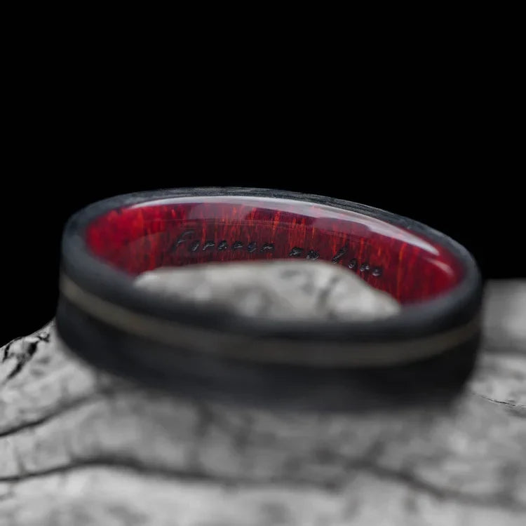 Forged wedding band with meteorite and guitar string inlay, featuring a bloodwood inner sleeve, mens matte flat profile 6mm ring, showcased on a white sea branch, available with free engraving.