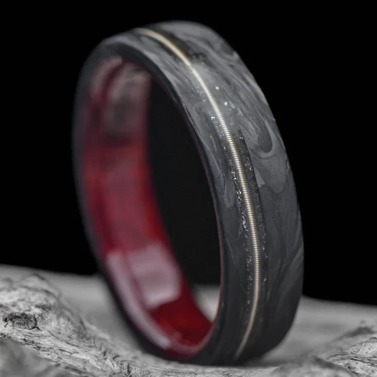 Mens 6mm matte flat profile forged wedding band with meteorite and guitar string inlay, featuring a bloodwood inner sleeve, displayed on a white sea branch, offering free engraving.