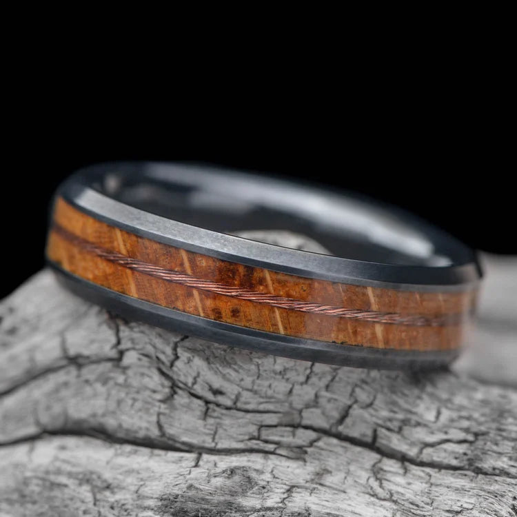 Black titanium mens wedding band with whiskey barrel oak and stranded copper wire inlays, 6mm, displayed on a white sea branch, unique design, free engraving available.