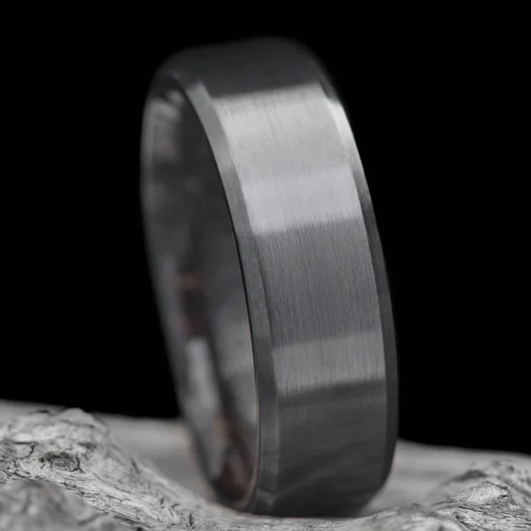 Black titanium wedding band for men with brushed bevel profile, featuring a unique T-Rex inner sleeve design, 8mm width, displayed on a white sea branch, free engraving available.